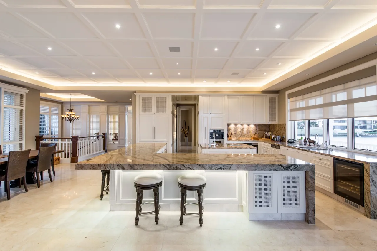 Kitchen with a large stone island, white cabinetry and a coffered, lit ceiling
