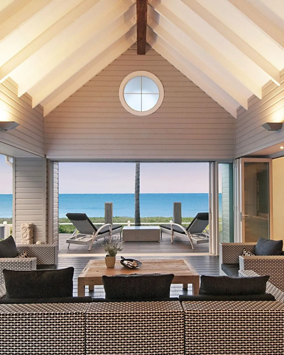 Beachfront living room with dark wicker sofas opening to the ocean under a vaulted ceiling