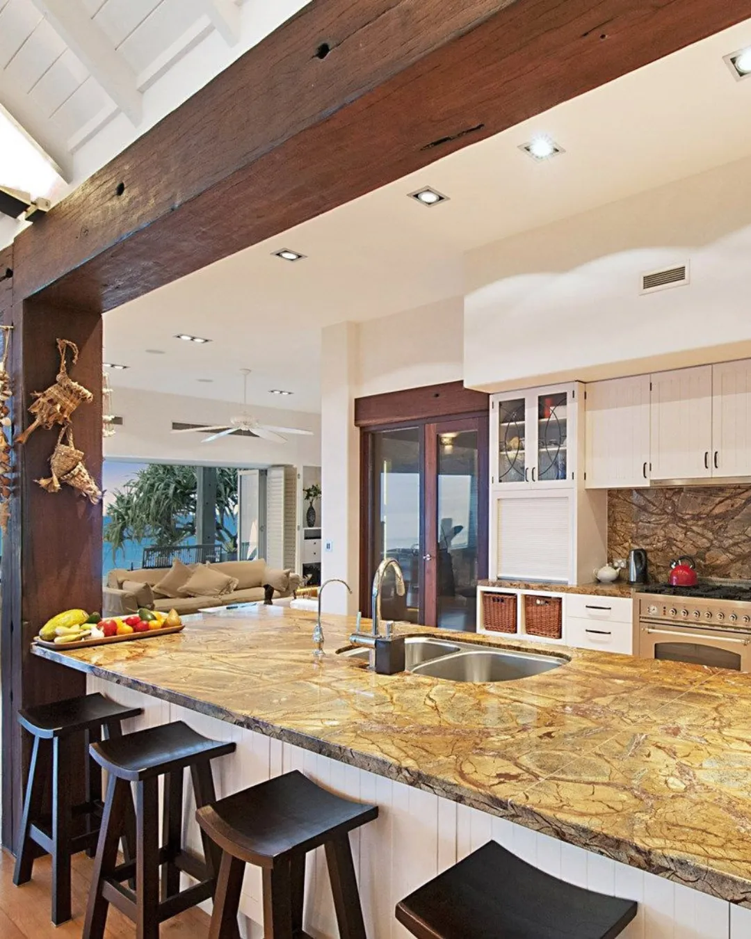 Kitchen with a polished stone benchtop, black bar stools and a reclaimed timber beam