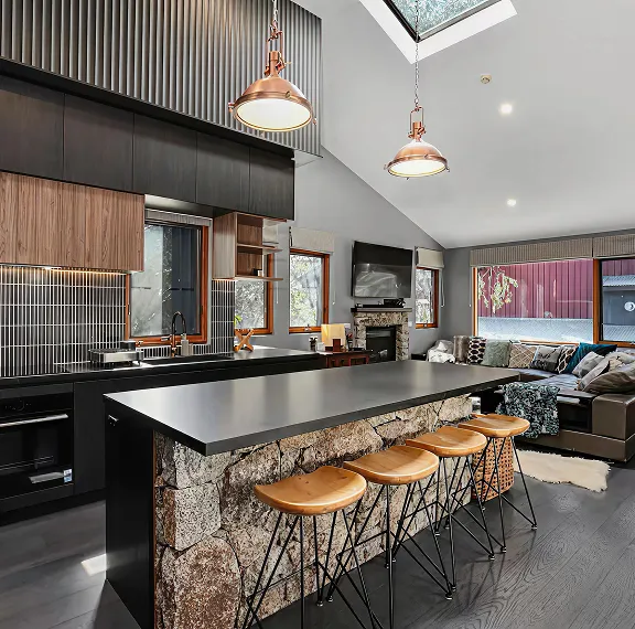 Open-plan kitchen with a stone-clad island, tan bar stools and copper pendant lights