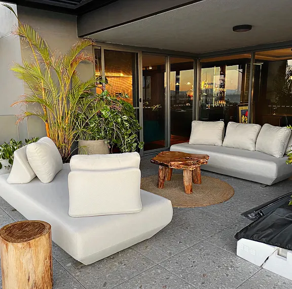 Lounge with a cream sofa, a driftwood coffee table and tropical plants beside glass sliding doors