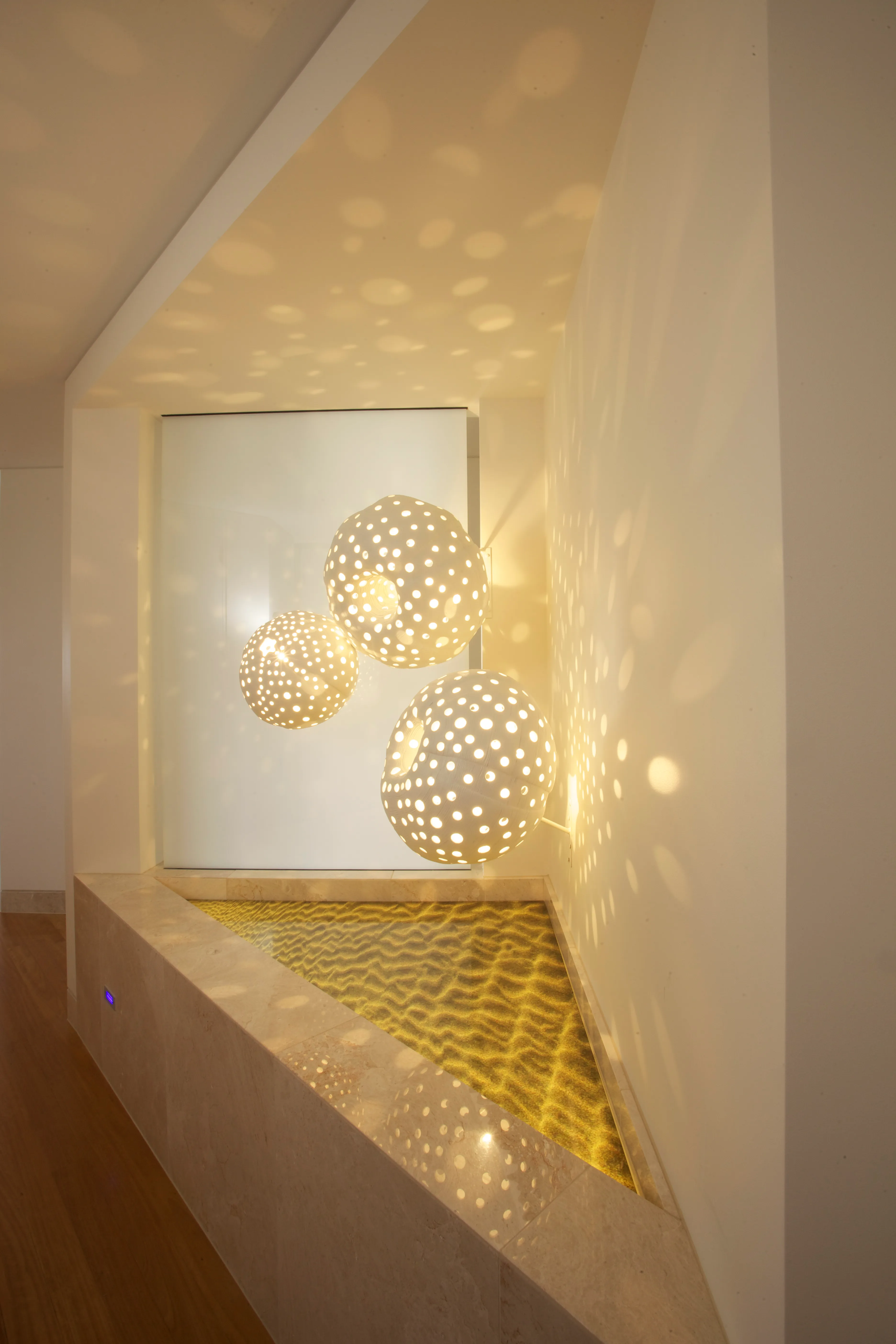 Wall niche lit by perforated globe pendants casting patterned light over a sand-textured floor
