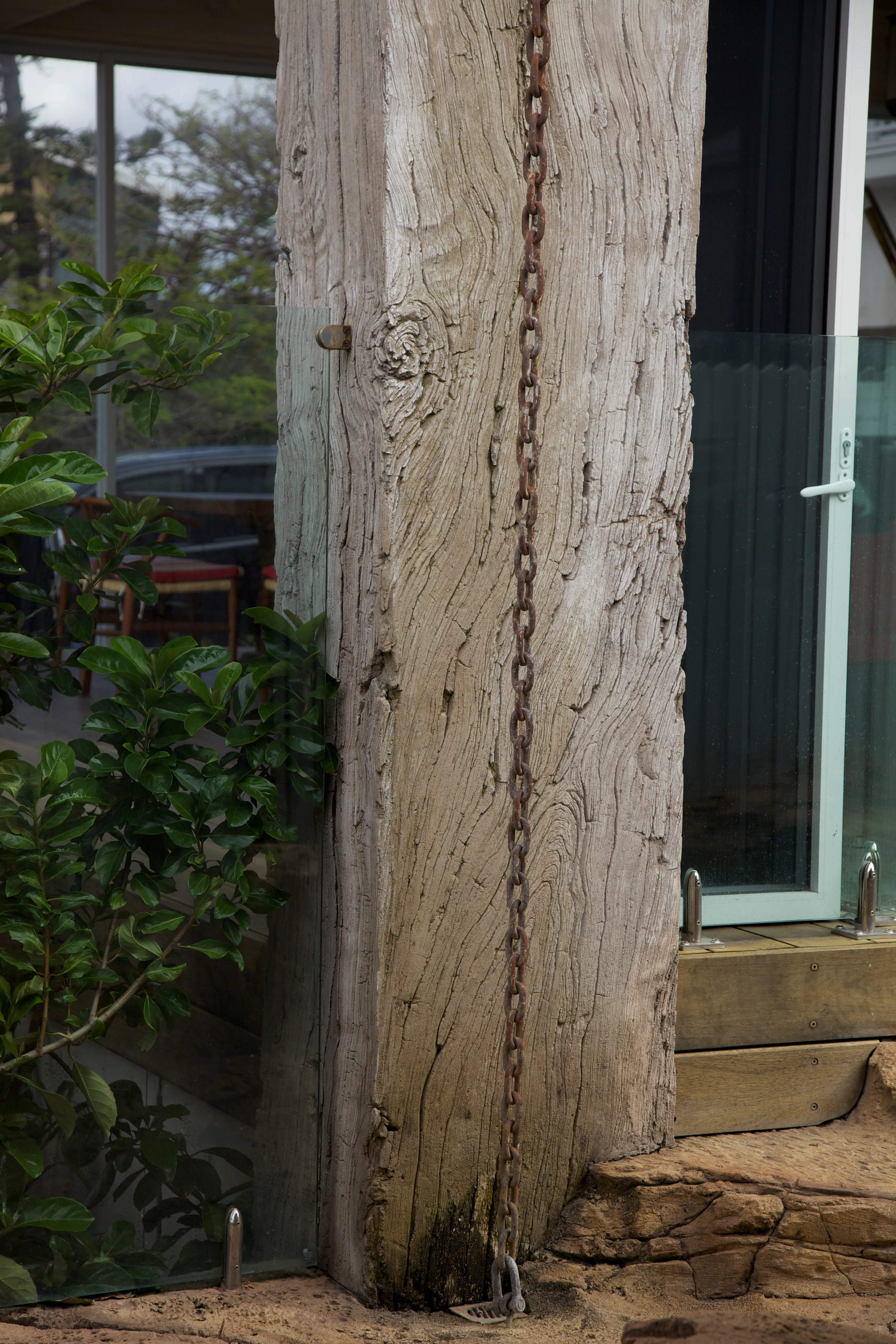 Weathered timber post with an iron chain beside a window and garden greenery