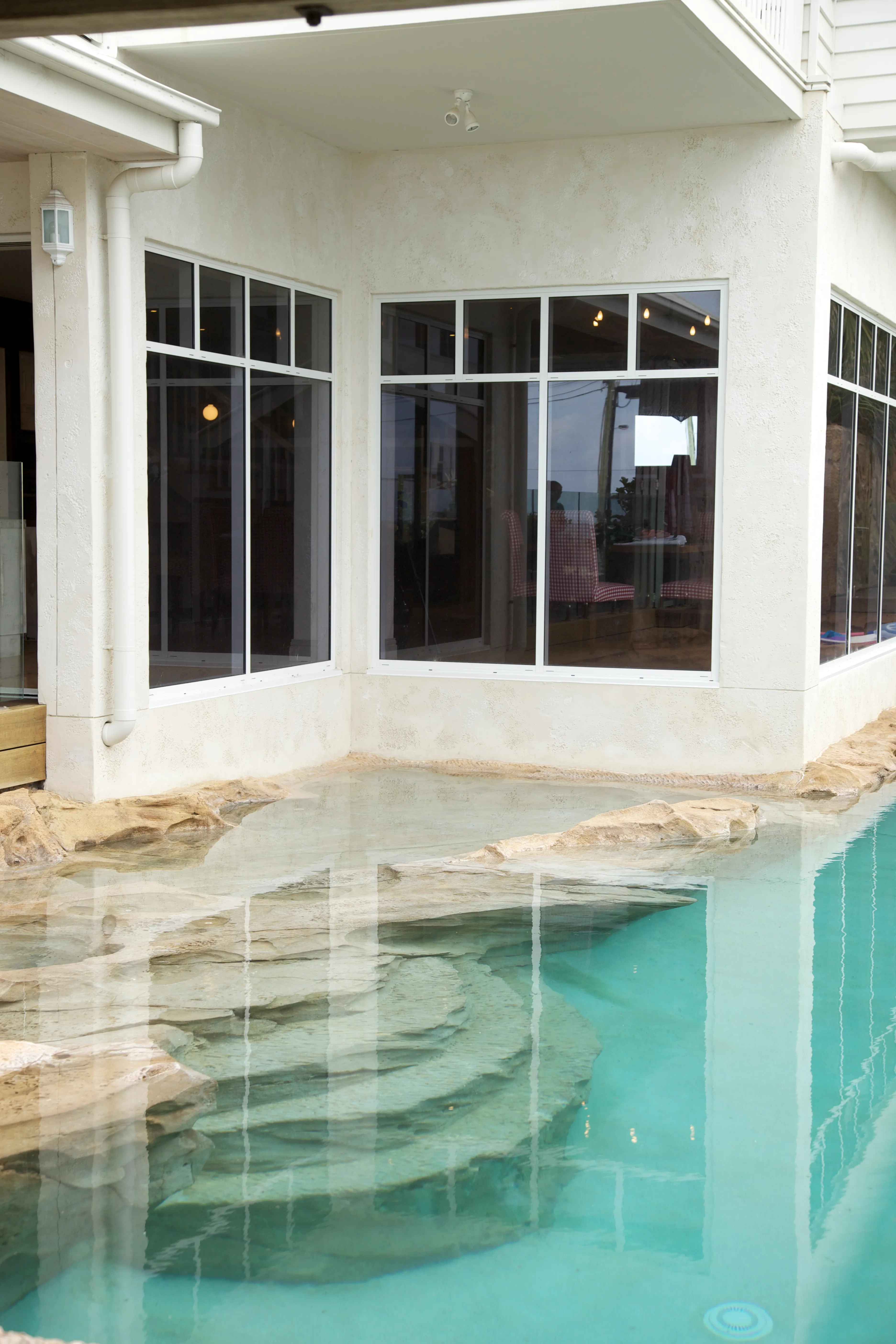 Rendered home corner with black-framed windows above a stepped, glass-clear pool