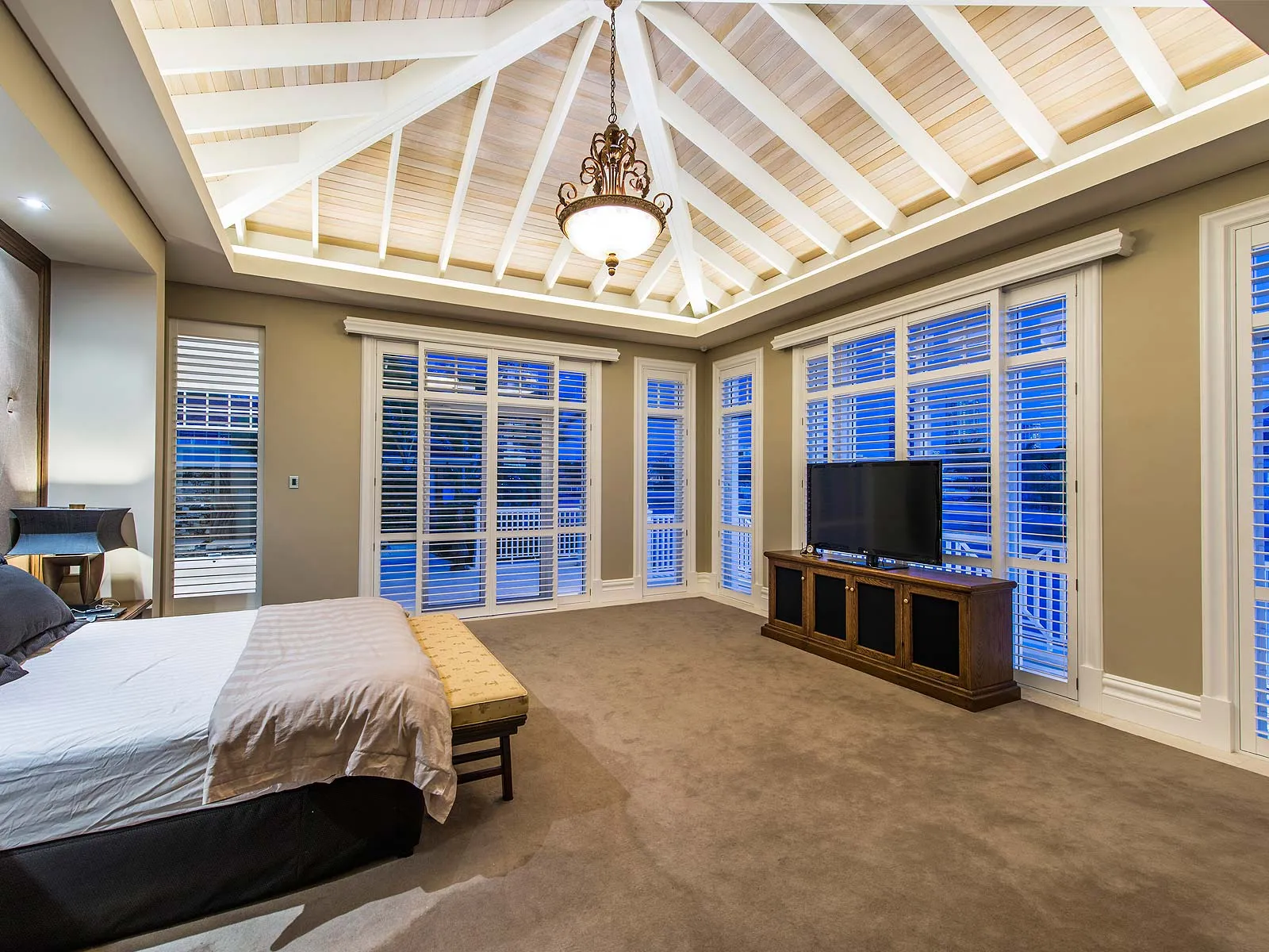 Main bedroom with a vaulted white-beamed ceiling, plantation shutters and a carved timber media unit
