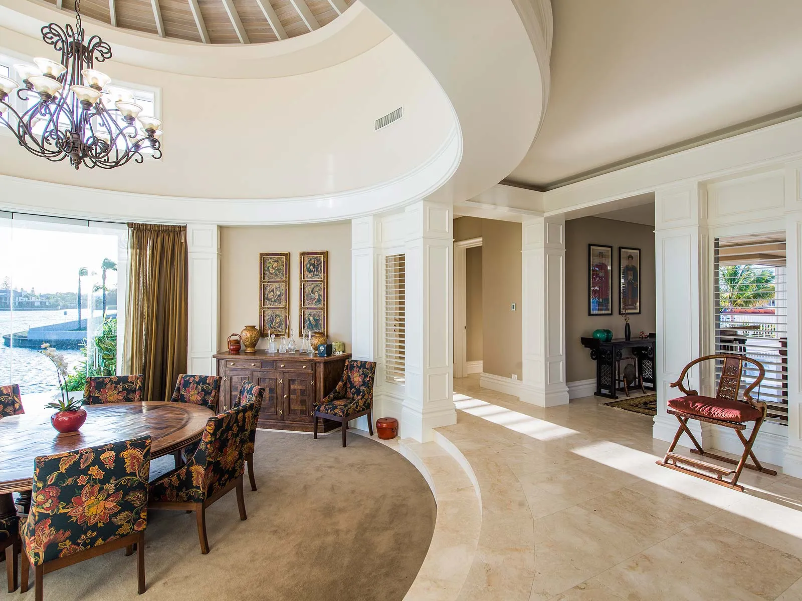 Curved dining room with a chandelier, floral-upholstered chairs and a view over the water