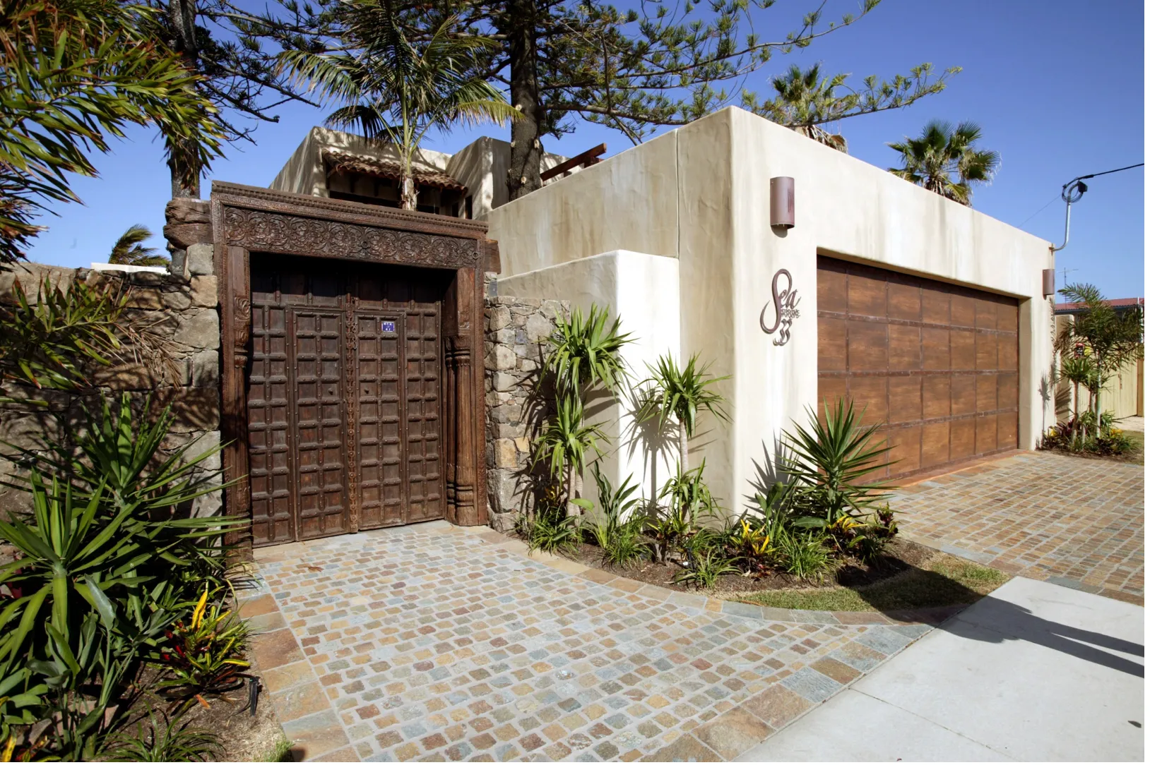 Entry courtyard with carved timber doors, a white rendered wall and cobblestone paving