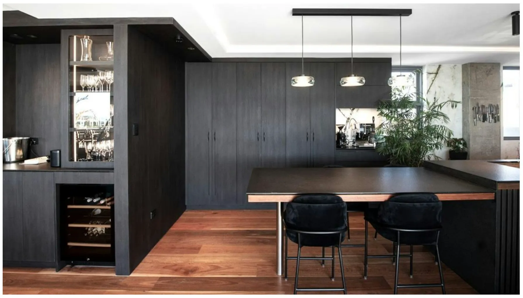 Dark timber kitchen with a wine fridge, glass pendants and a long island with black chairs