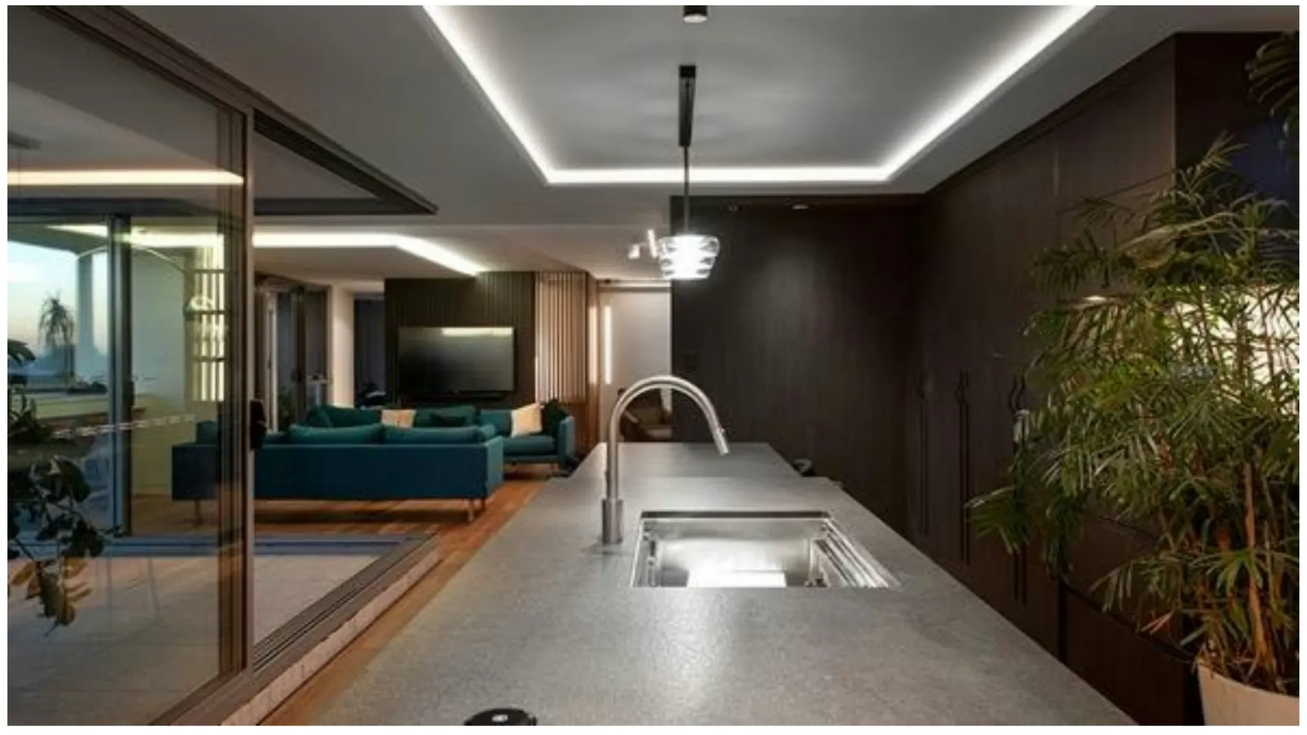 Kitchen sink on a stone island looking toward a teal sofa through a glass sliding door