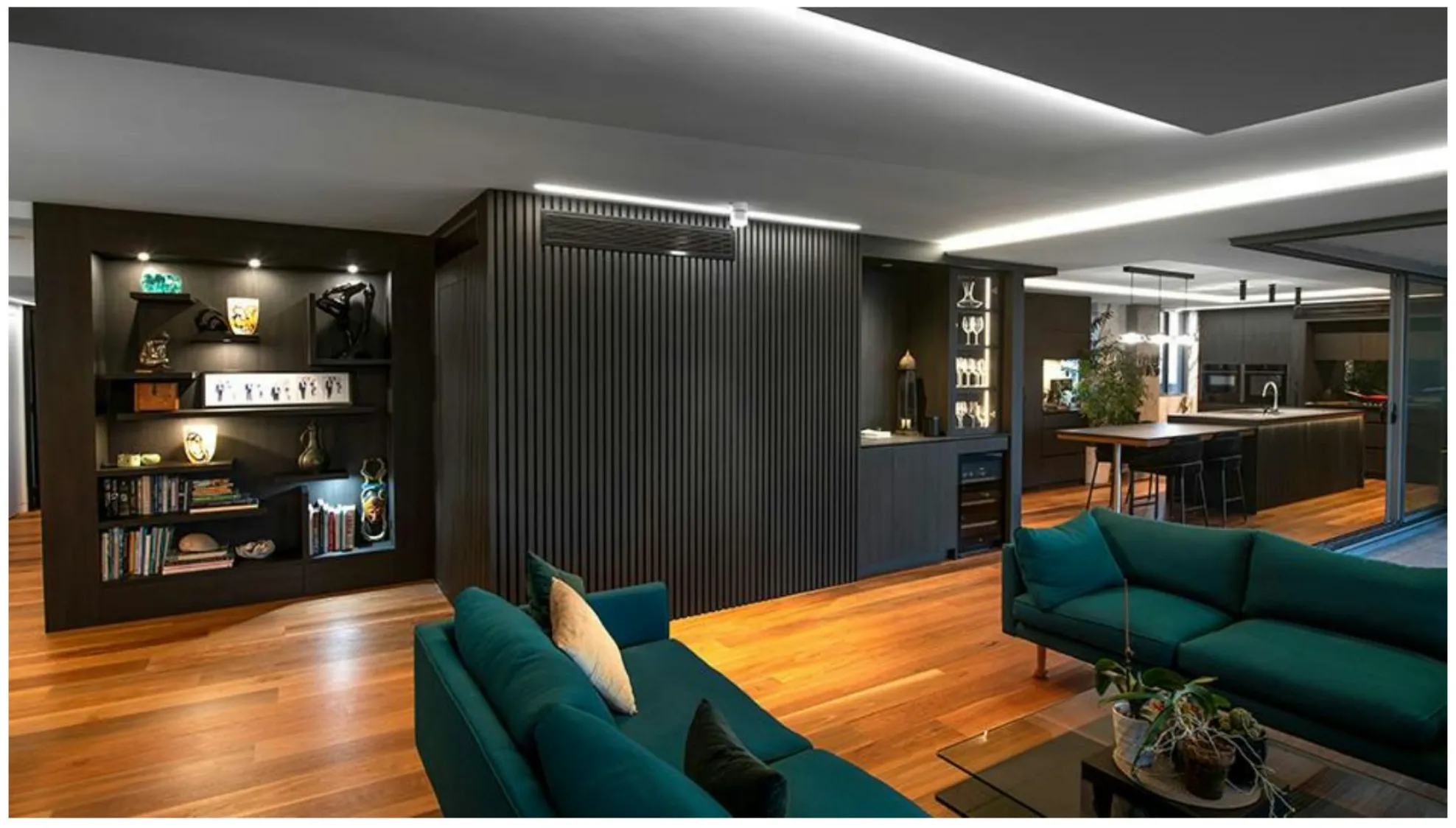 Open living area with teal sofas, black joinery with open shelving and a lit ceiling edge