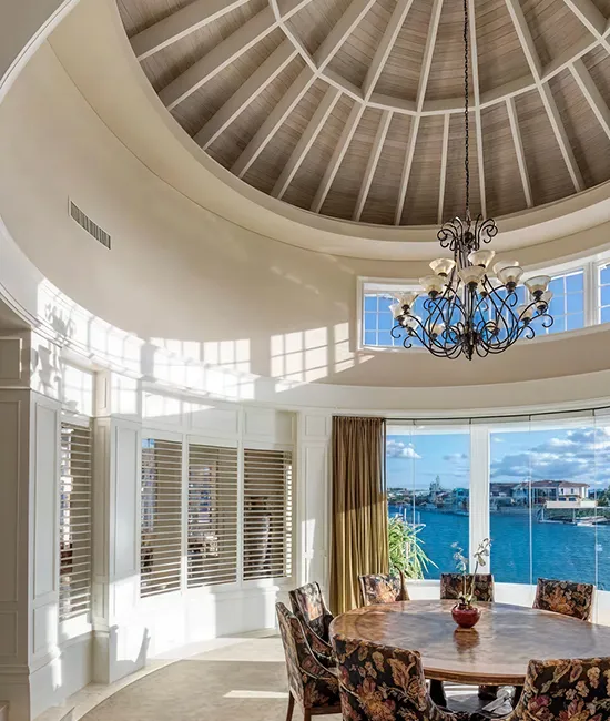 Round entry hall with a domed timber ceiling, chandelier and a dining table by the waterfront windows