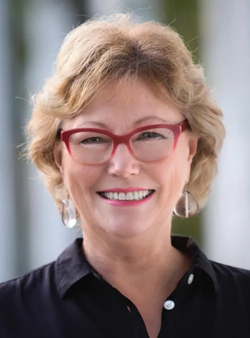 Portrait of the designer, smiling, wearing red-framed glasses and a dark shirt