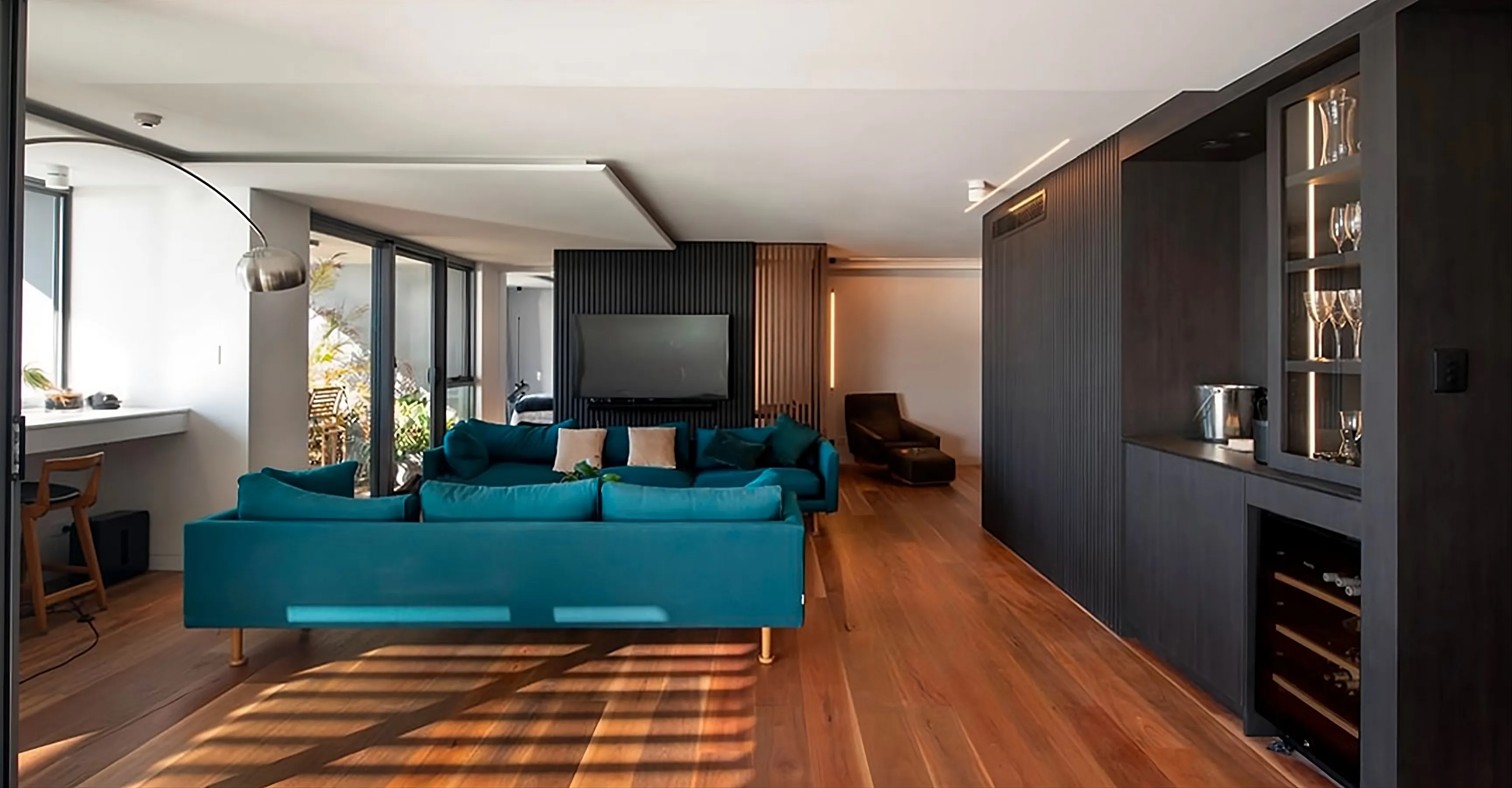 Living room with a teal sofa, black joinery and timber floors lit by afternoon sun